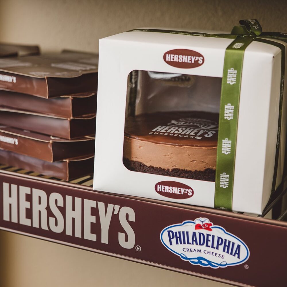 A box with a cheesecake inside that has the Hershey's logo and the Philadelphia cream cheese logo.